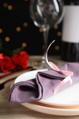 Beautiful place setting for romantic dinner on table against black background with blurred lights, closeup. Valentine's day celebration