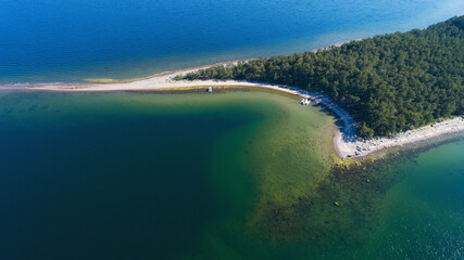 Aerial view on beautiful bay at sunny day with sandy beach and white yacht. Paradise island covered with pine trees. Finland. 