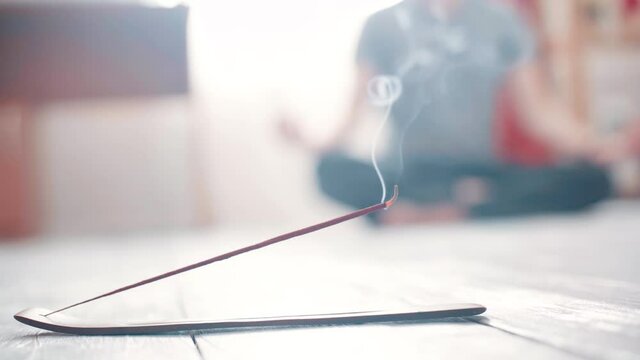 Steaming incense stick close-up on the floor and yogi in the background