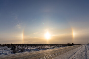 Snowy deserted road in winter on the orange a natural phenomenon halo glow background