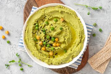 Spicy hummus of green peas and chickpeas in a white bowl on a grey background top view. Healthy appetizer, vegan food, vegetarian snack. 