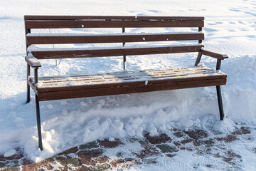 Wooden painted yellow color beautiful bench with white snow is in a park in winter in a sunny day