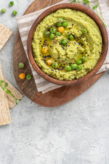Spicy hummus of green peas and chickpeas in a wooden bowl on a grey background top view. Healthy appetizer, vegan food, vegetarian snack. Copy space for text