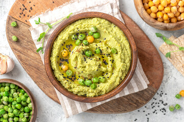 Spicy hummus of green peas and chickpeas in a wooden bowl on a grey background top view. Healthy appetizer, vegan food, vegetarian snack. 