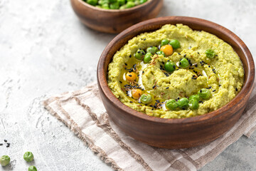Spicy hummus of green peas and chickpeas in a wooden bowl closeup. Healthy appetizer, vegan food, vegetarian snack. Puree of green peas, chickpeas, olive oil, garlic, and cumin.