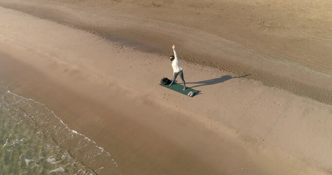 mujer mediana edad realizando estiramientos en la orilla del mar y dron sobrevolando