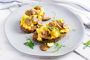 Scrambled eggs and fried mushrooms on bread. Homemade breakfast or brunch meal - scrambled eggs and mushrooms sandwiches.