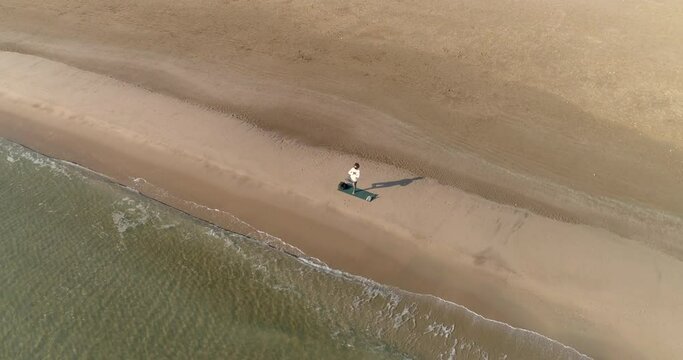 playa solitaria con mujer meditando haciendo posturas de yoga y vista dron cenital