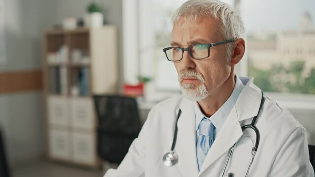 Experienced Middle Aged Male Doctor Wearing White Coat Working on Personal Computer at His Office
