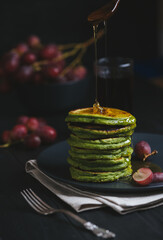 Green pancakes with matcha tea or spinach, dressed honey and red grapes. Ideas and recipes for healthy breakfast with superfood ingredients. Dark background - 409083275