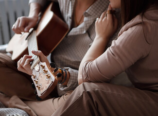 Man playing acoustic guitar at home with woman sitting on bed cozy love