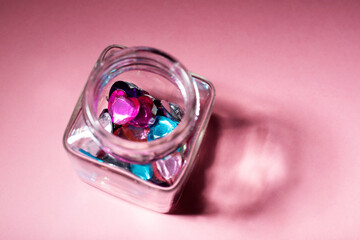 glass jar with colored plastic heart on pink background