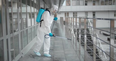Worker in virus protective suit and mask disinfecting building of coronavirus with sprayer
