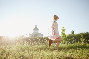 Blonde girl in pink linen dress spins in the field of flowers summer and sunlight