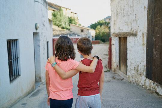back view of kids walking embraced along the street in a Spanish village in Teruel with a bullring in the background