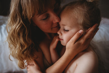 Gorgeous mother and daughter with closed eyes kissing at home