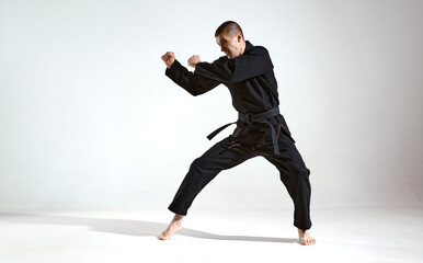 Fighting man in black kimono fighter shows karate technique on studio background with copy space,...
