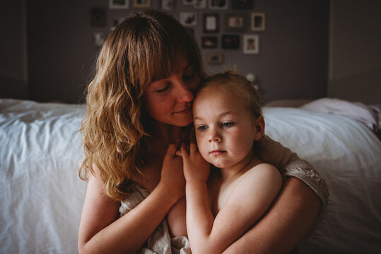 Mother with closed eyes while hugging daughter in bedroom