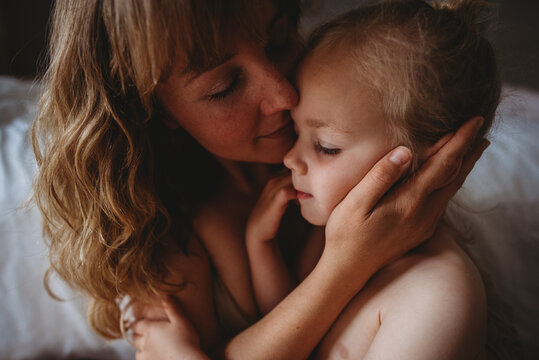 Gorgeous mother and daughter with closed eyes kissing at home