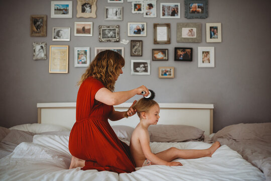Mother brushing daughter's hair in family bed with photos on wall - Powered by Adobe