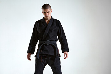 Sportive frowning man in black kimono for karate or kudo on white studio background with copy space