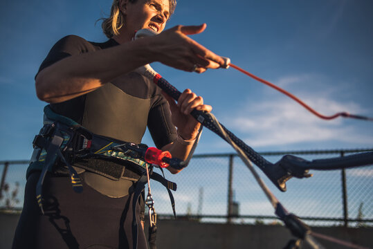 A woman in a wetsuit rigs up her kite on the beach before kiteboarding
