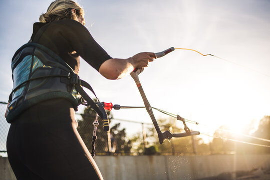 A woman in a wetsuit rigs up her kite on the beach before kiteboarding