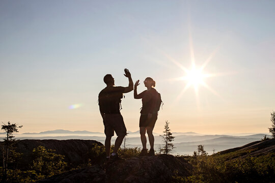 Two hikers high five and celebrate reaching summit of mountain, Maine
