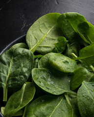 Baby spinach leaves with water drops in a ceramicn plate on a black background.