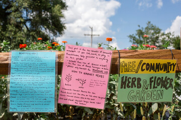Colorful signs on a community garden fence against a bright blue sky