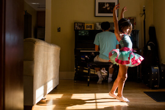 A little girl in tutu raises her arm to dance to father's piano music