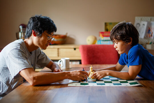 A father and son sit together at a table playing a game of chess