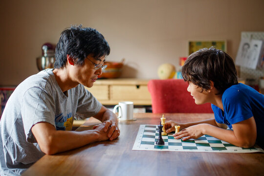 A boy makes chess move while playing with father at dining room table