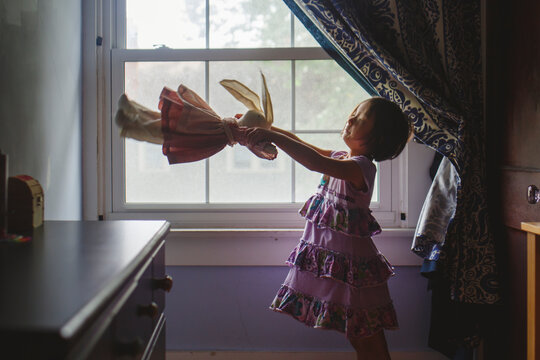 A cute little girl stands by window playing with a soft stuffed animal