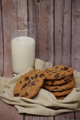 A stack of homemade chocolate chip cookies on a dishtowel with a glass of milk