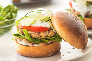 Homemade salmon burger with fresh vegetables served on a white plate.
