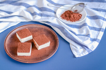 Still life with square souffle bird milk sprinkled with cocoa on a blue background top view