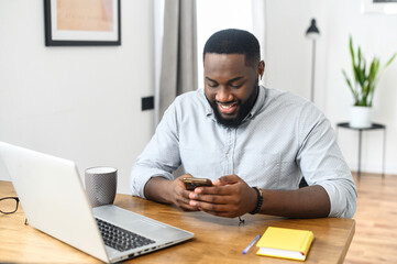 Smiling young african american hipster business man professional making business, looking on the phone, enjoying corporate mobile conversation indoors, freelance work from home