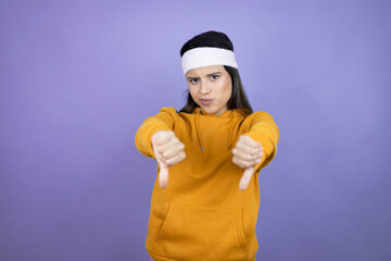 Young latin woman wearing sportswear over purple background with angry face, negative sign showing...