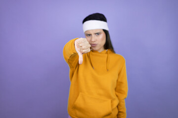 Young latin woman wearing sportswear over purple background with angry face, negative sign showing dislike with thumbs down