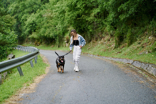Young woman with blonde braided hair wearing a denim jacket and white jean walking her dog on a rainy day