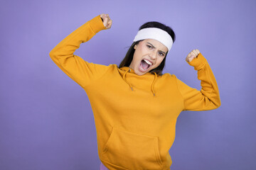Young latin woman wearing sportswear over purple background very happy and excited making winner gesture with raised arms, smiling and screaming for success.