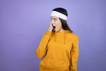 Naklejka na ściany i meble Young latin woman wearing sportswear over purple background covering mouth with hand, shocked and afraid for mistake. surprised expression