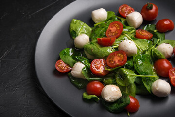 Salad with mozzarella and baby spinach on black ceramic plate