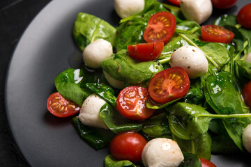 Salad with mozzarella and baby spinach on black ceramic plate