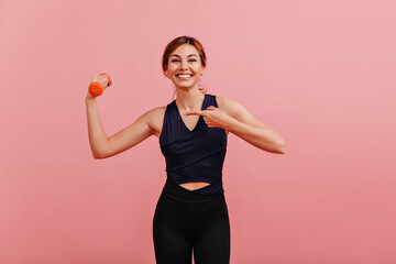 Happy positive lady in black sports leggings shows perfect tight body and strong arms holding weight