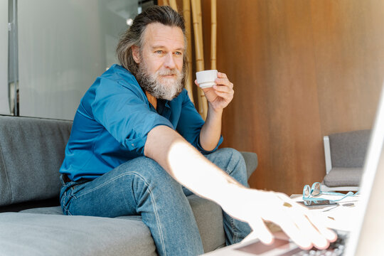 Mature man with a beard drinking a cup of coffee and talking on a vide