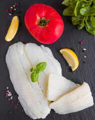 Raw halibut fish fillet, tomato, lemon basil and spices on black stone board, top view - 409092281
