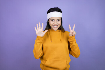 Young latin woman wearing sportswear over purple background showing and pointing up with fingers number seven while smiling confident and happy