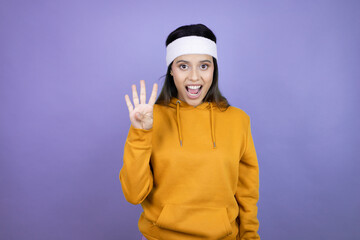 Young latin woman wearing sportswear over purple background showing and pointing up with fingers number four while smiling confident and happy